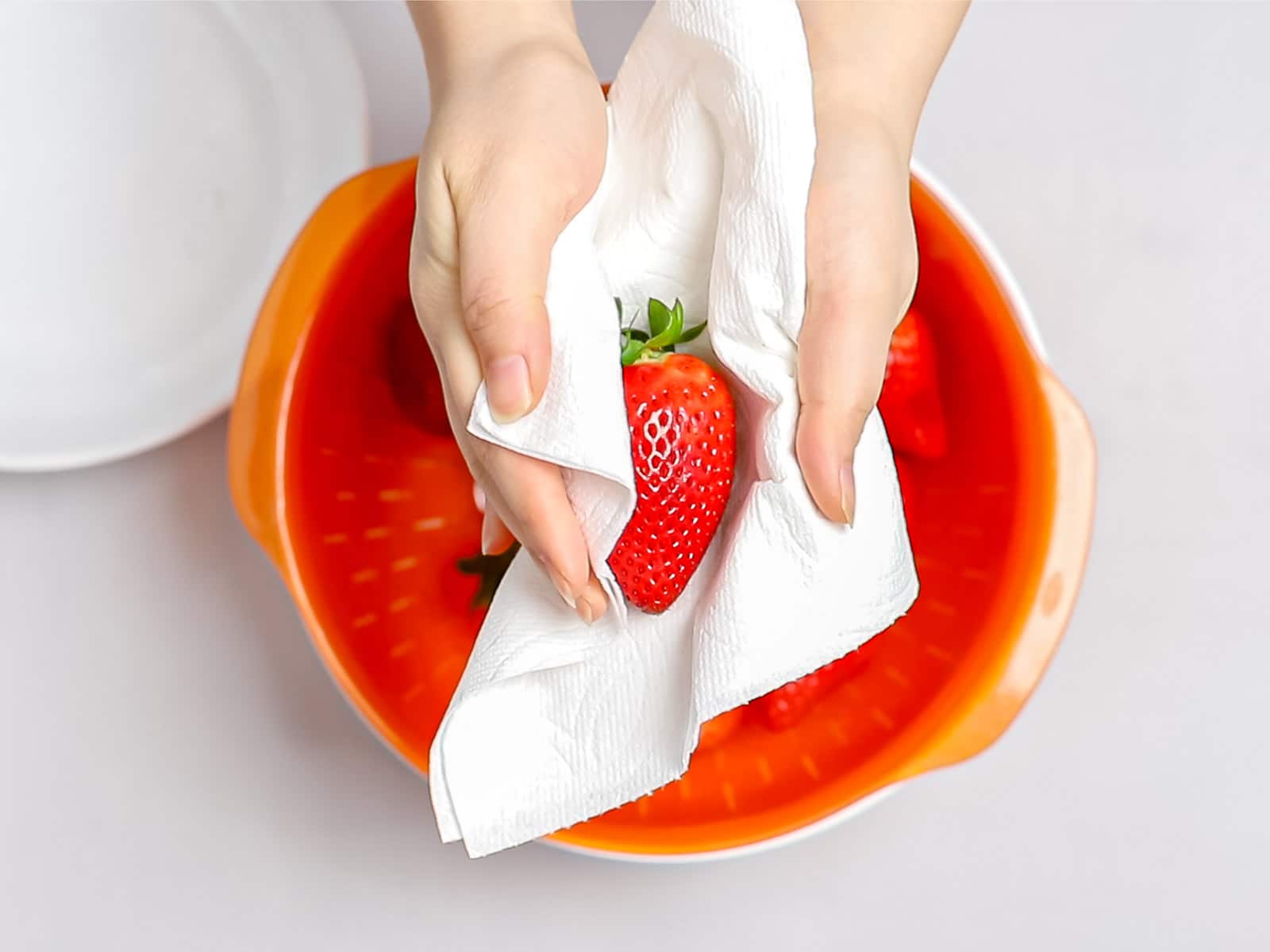 a strawberry being dried with a paper towel over an orange colander