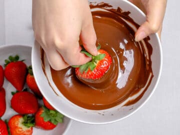 hand dipping a strawberry in melted chocolate