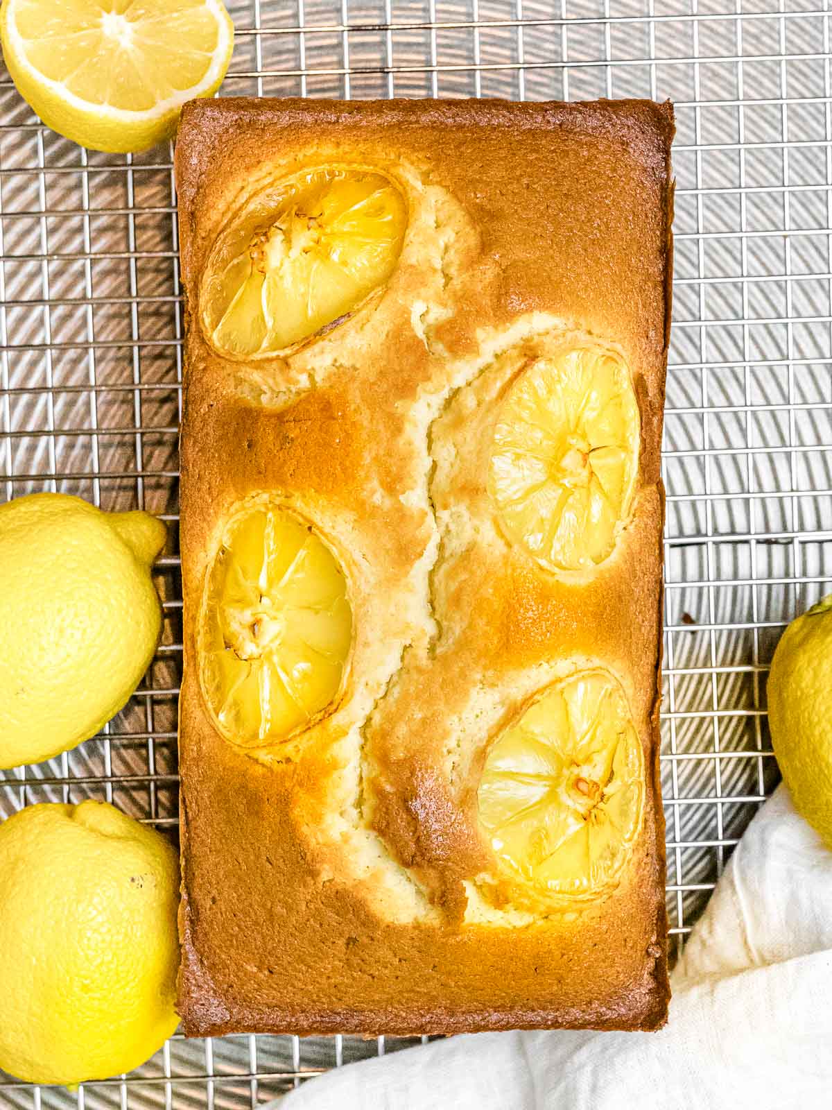 lemon pound cake with golden brown crust topped with four slices of lemon on a cooling rack