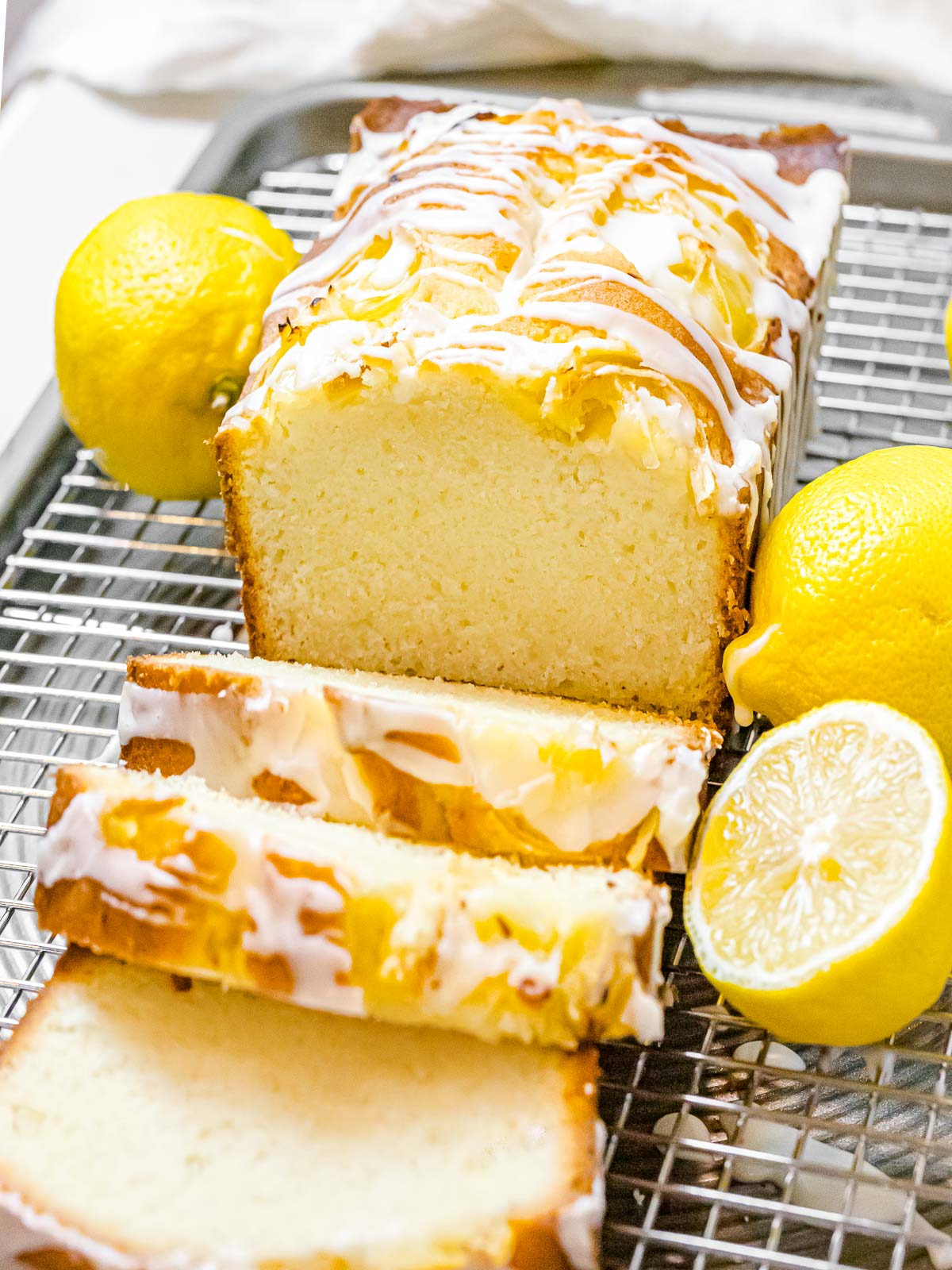 moist lemon pound cake glazed with icing sliced open on a metal rack next to lemons