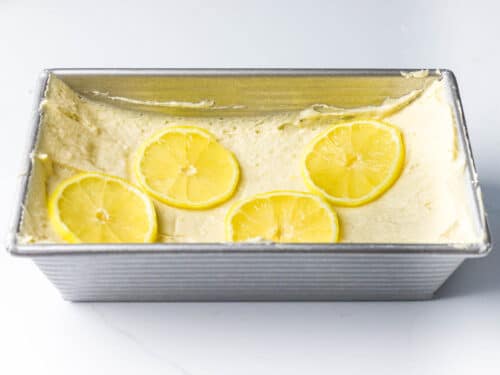 pound cake batter made into a well topped with thin lemon slices in a metal loaf pan
