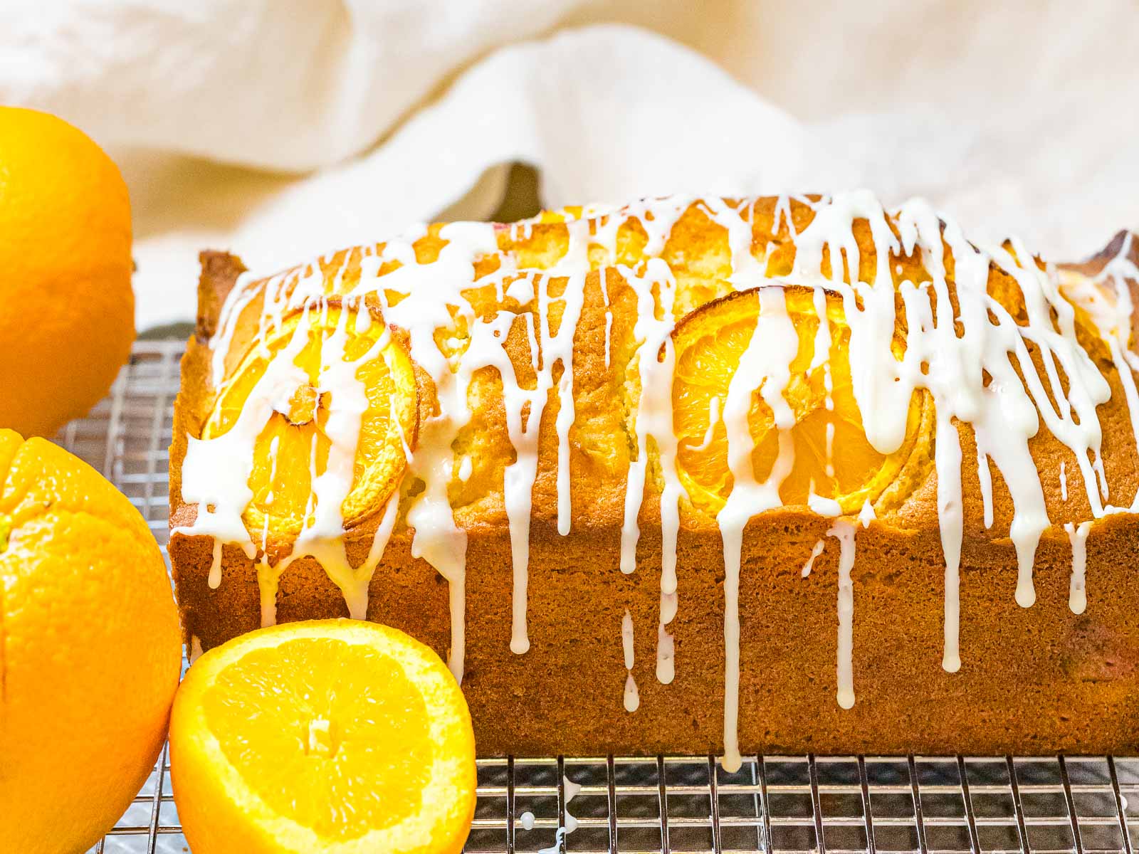 orange pound cake with glaze drizzled on top and falling down the sides next to oranges