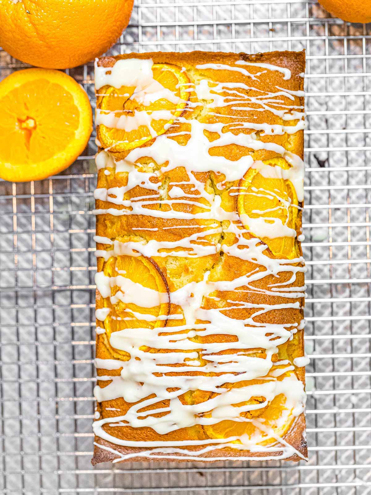 orange pound cake with glaze drizzled on top and decorated with oranges on top of a metal wire rack