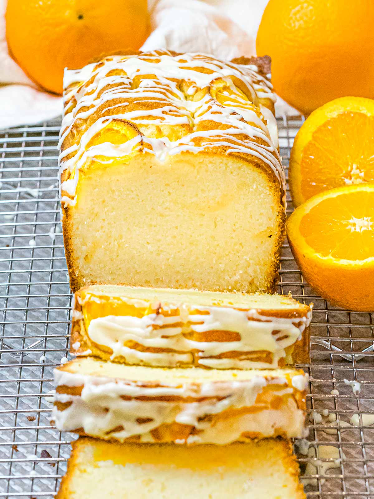 golden brown orange pound cake with icing glaze cut into slices next to oranges