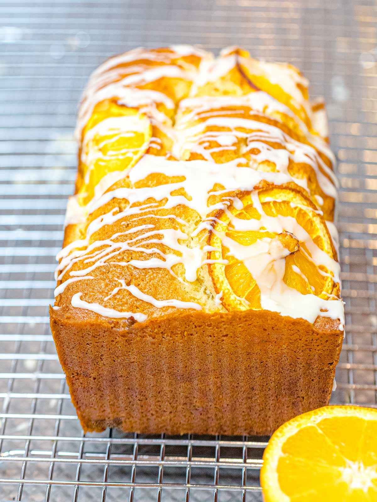 loaf of orange pound cake with a glazed icing drizzle topped with orange slices on a wire cooking rack