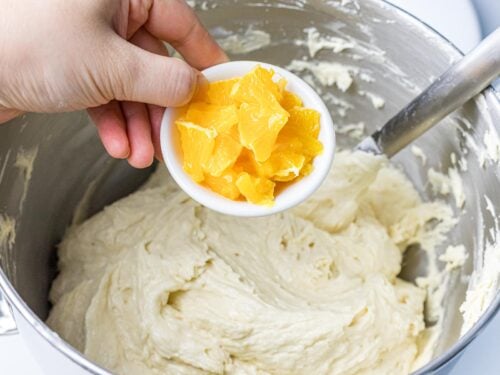 chopped up orange segments being added to pound cake batter in a metal bowl