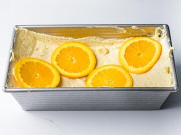 orange pound cake batter in a loaf pan with a well in the center with orange slices placed on top