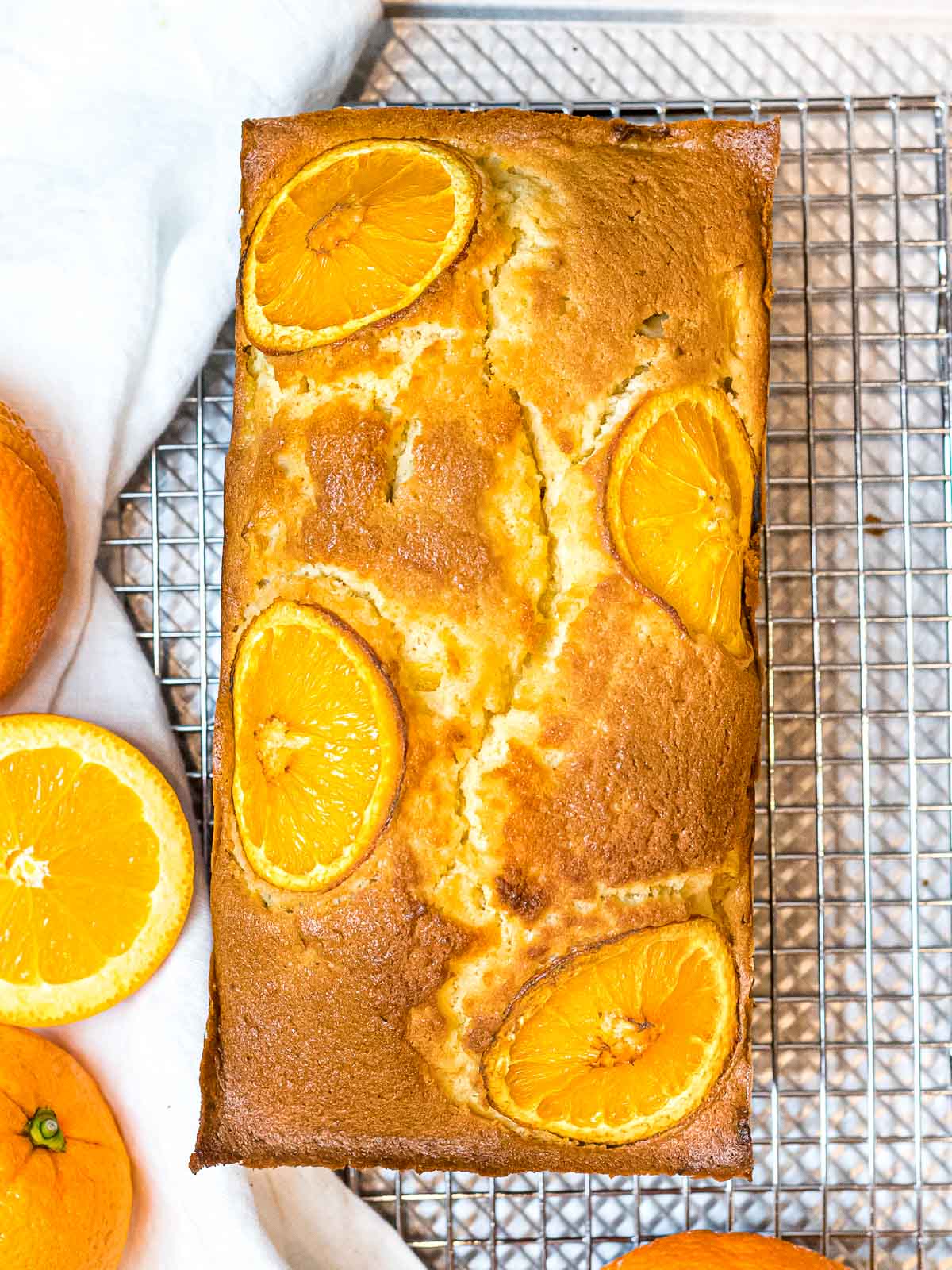 orange pound cake with a golden brown crust and decorated with orange slices placed on a wire rack next to oranges