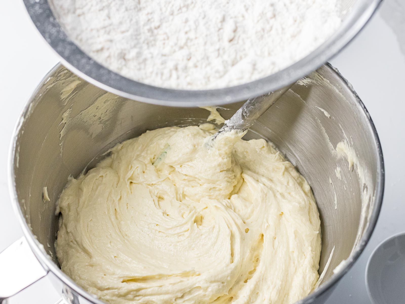 pound cake batter in a metal bowl with flour being added from a sifter