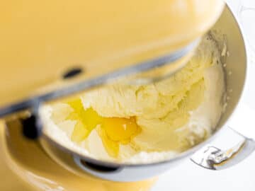 one egg added to fluffy, creamy pound cake batter in a yellow stand mixer bowl