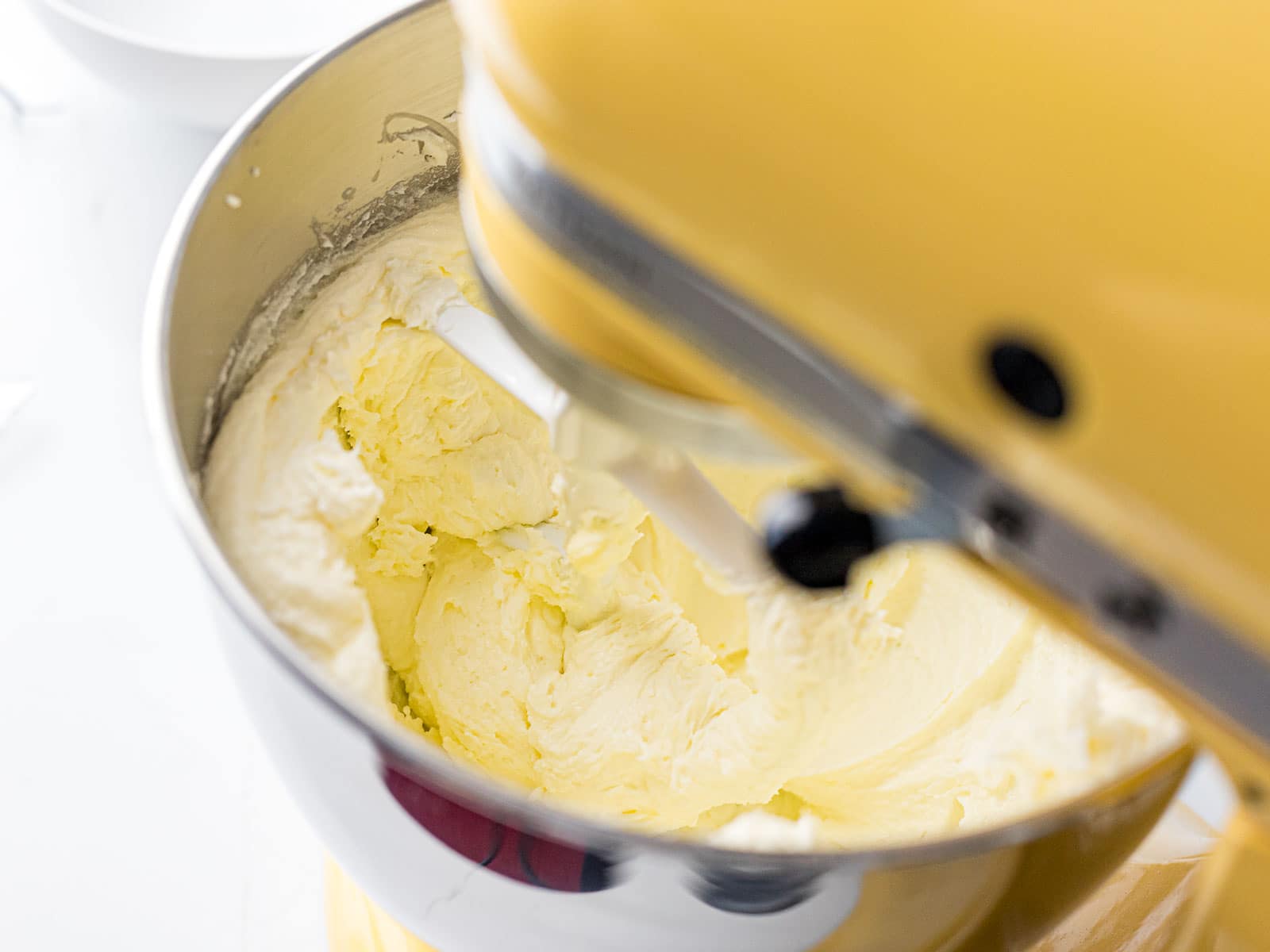 fluffy pound cake batter being mixed in a yellow stand mixer with a paddle attachment