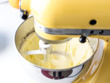 butter and sugar being creamed in a yellow stand mixer with a paddle attachment