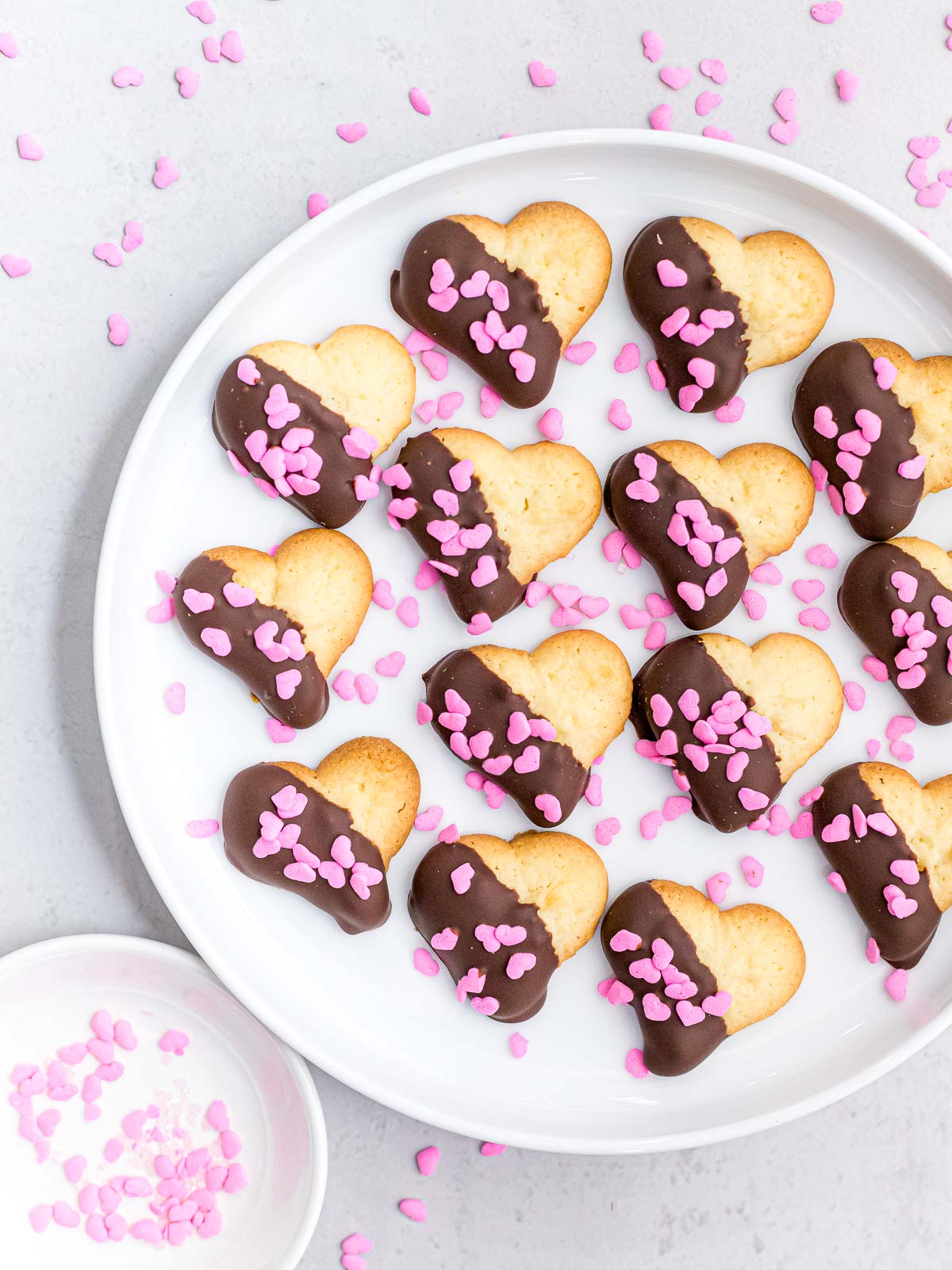 Valentines spritz cookies dipped in melted dark chocolate and decorated with pink heart shaped sprinkles