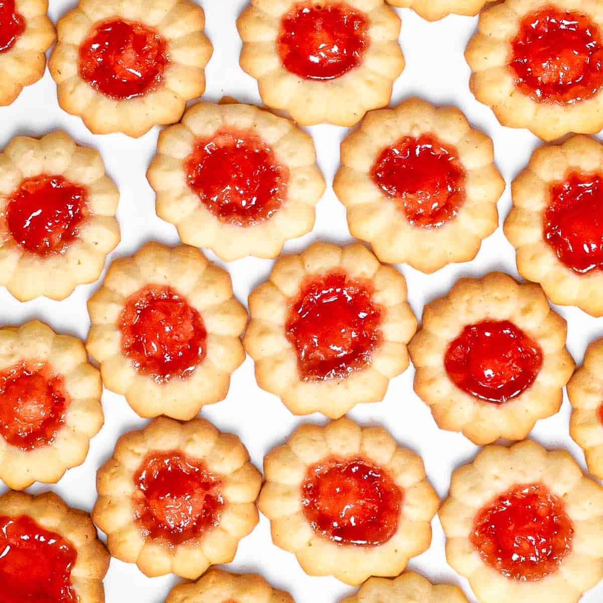 A close up of jam thumbprint cookies filled with red jam on a white surface.