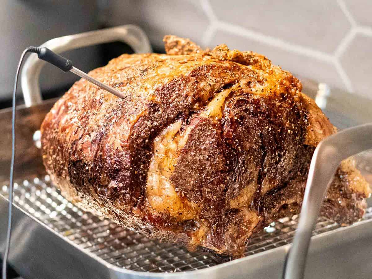 Prime rib roast with browned crust on a roasting pan with a meat thermometer inserted.