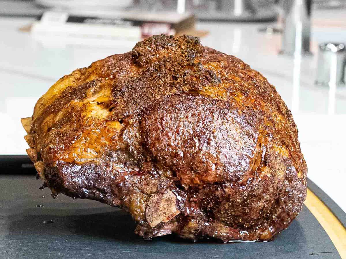 Standing rib roast laying bone side down on a black cutting board with a crunchy golden brown crust after reverse searing.