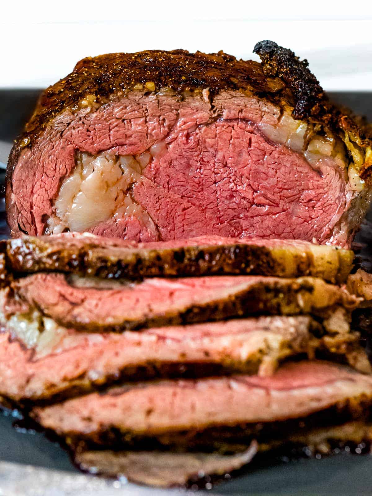 Carnivore recipes, Prime rib roast with brown crust cut into slices on a dark cutting board to reveal medium rare doneness.