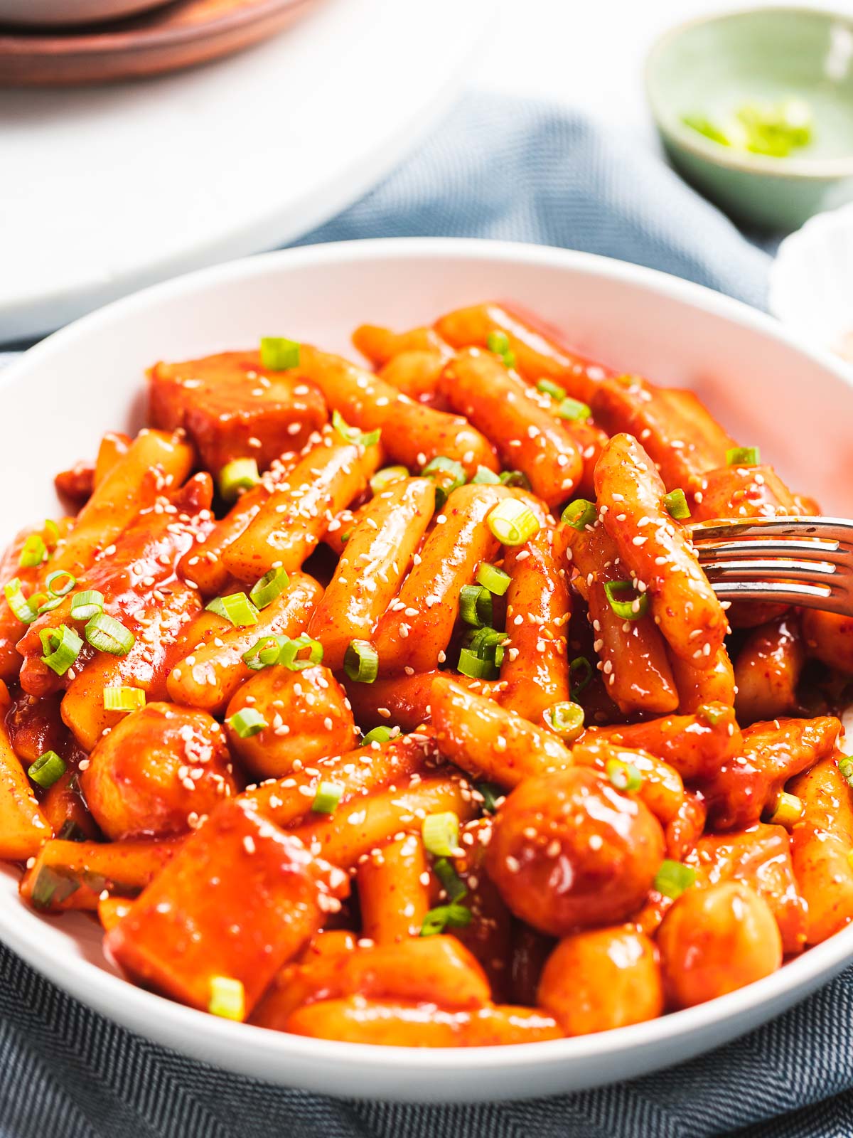 Tteokbokki made with gochujang and fish cakes garnished with scallions and sesame seeds.