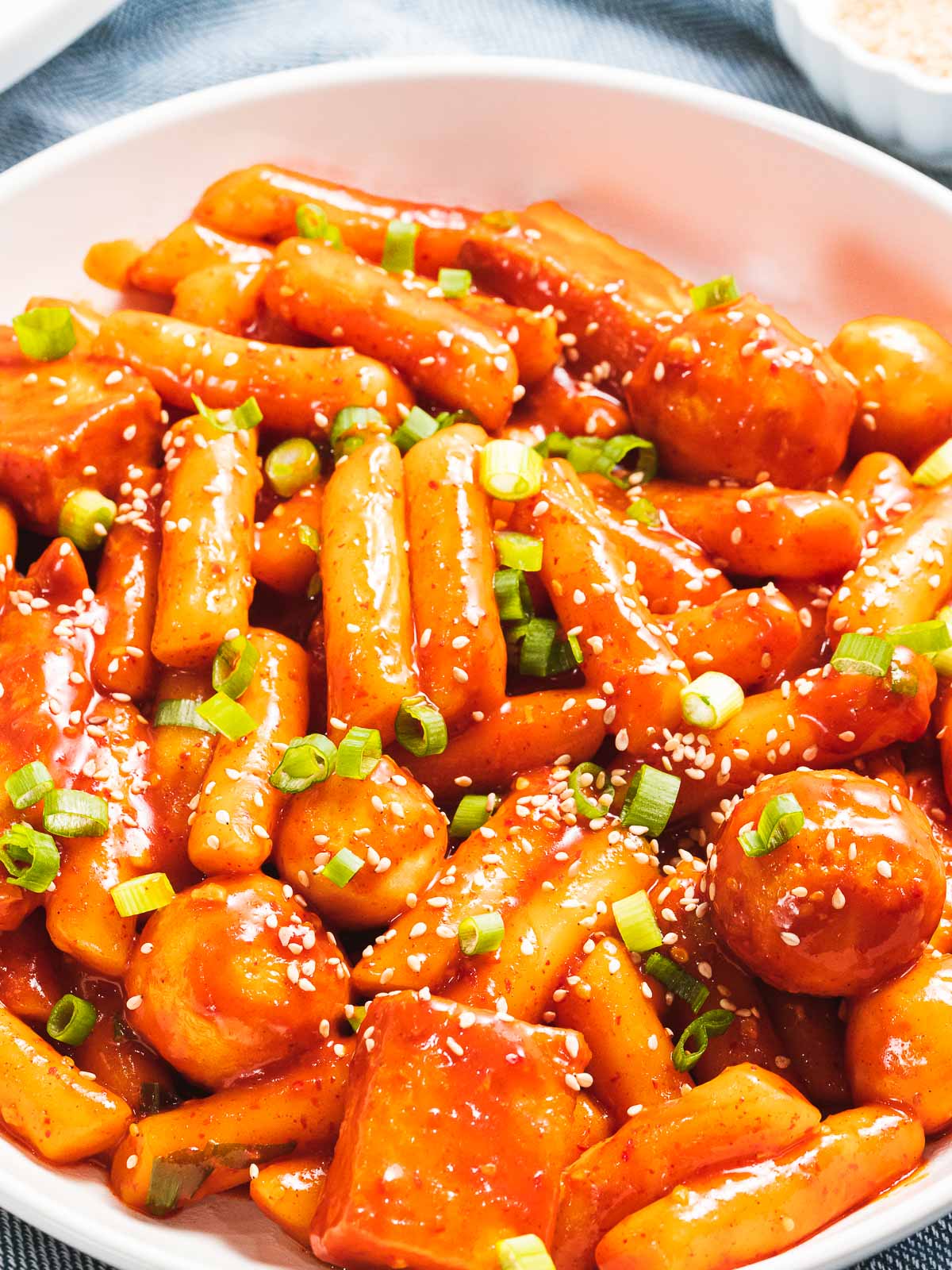 Tteokbokki made with gochujang and fish cakes garnished with scallions in a white bowl with red chopsticks.