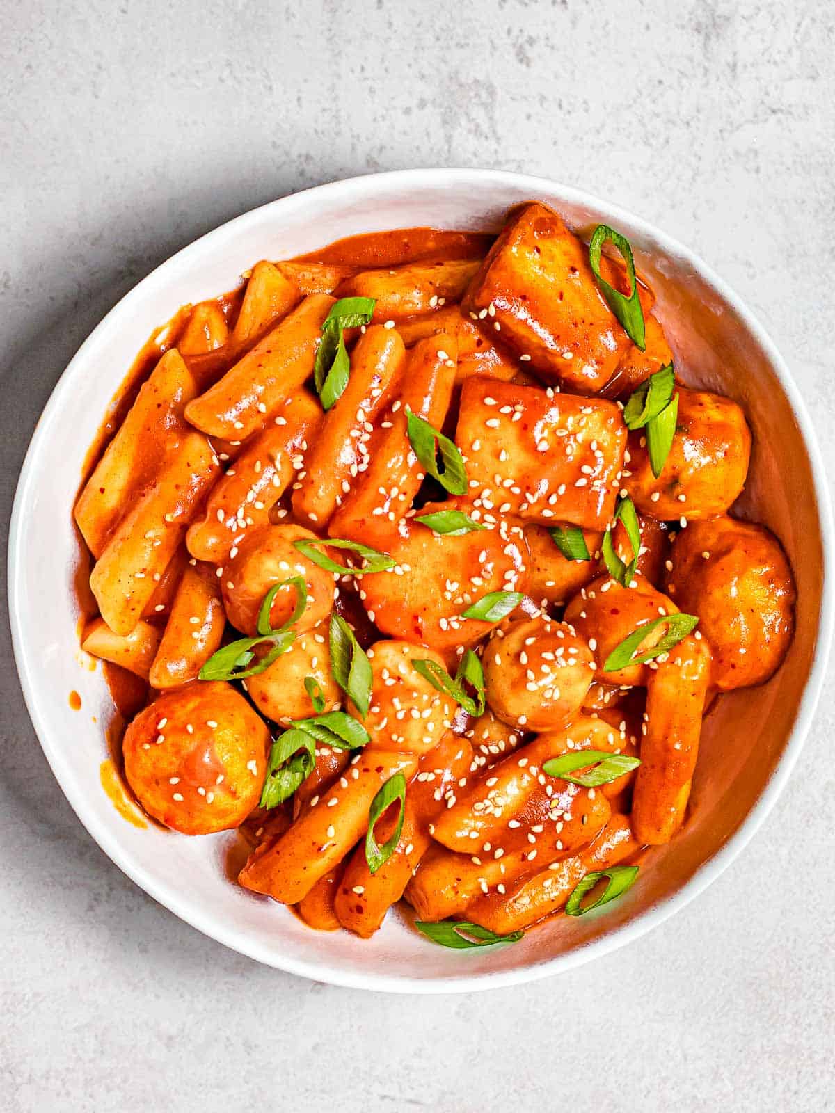 Spicy tteokbokki with fish cakes with scallions and sesame seeds.