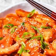 tteokbokki made with Korean rice cakes in a spicy sauce in a bowl next to chopsticks with text overlay