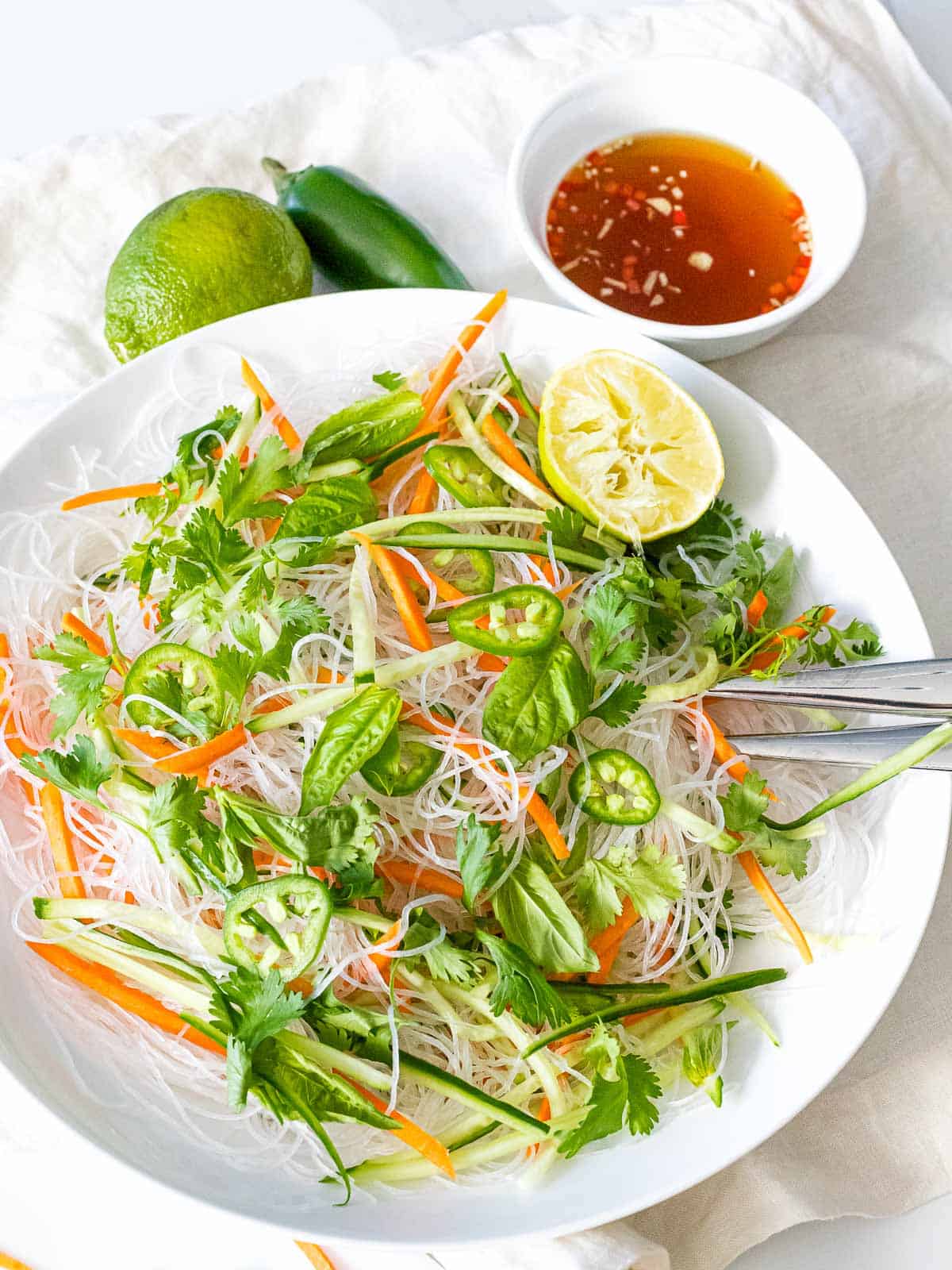 Vietnamese cold noodle salad tossed together with fresh herbs, jalapenos, carrots, and cucumber next to a bowl of tangy dressing.