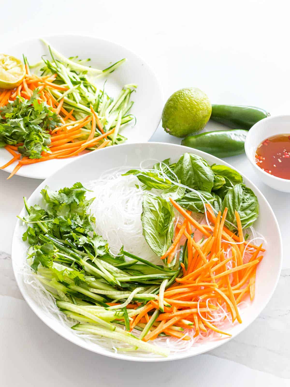 Vietnamese noodle salad with vermicelli rice noodles, basil, cilantro, carrots, and cucumbers next to a bowl of dressing.