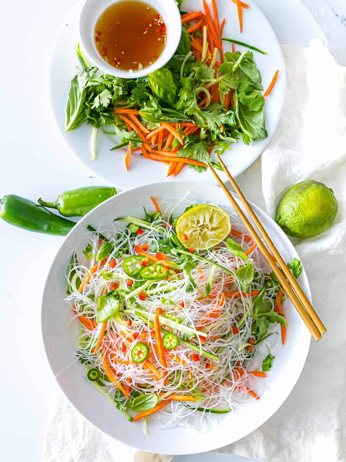 Vietnamese noodle salad with dressing made with vermicelli rice noodles, vegetables, lime, carrots, and fresh herbs in white bowl with wooden chopsticks.