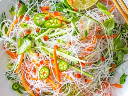 Vietnamese noodle salad with vermicelli rice noodles, lime, basil, vegetables, and dressing in a white bowl with chopsticks.