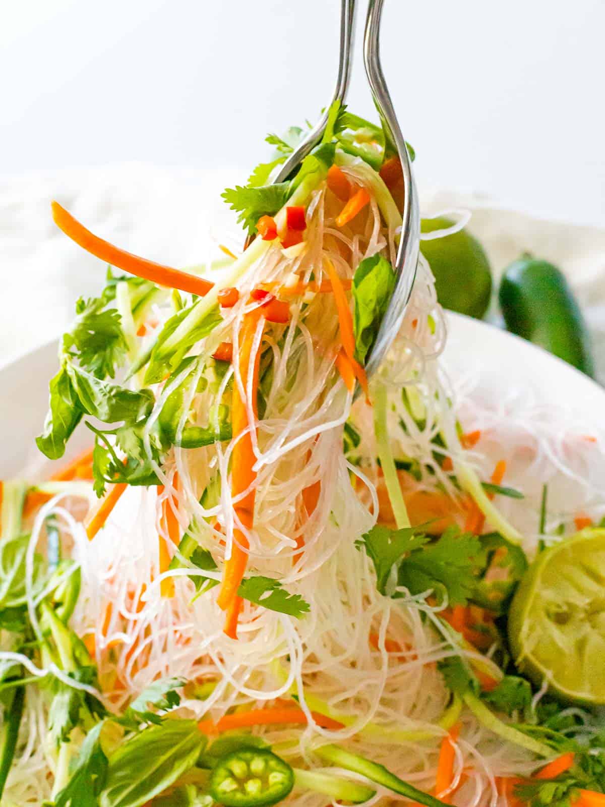 Vietnamese cold noodle salad with vermicelli rice noodles, basil, cilantro, carrots, and vegetables being served with silverware.