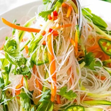Vietnamese noodle salad with vermicelli rice noodles, basil, cilantro, carrots, and green peppers being lifted from a white bowl.