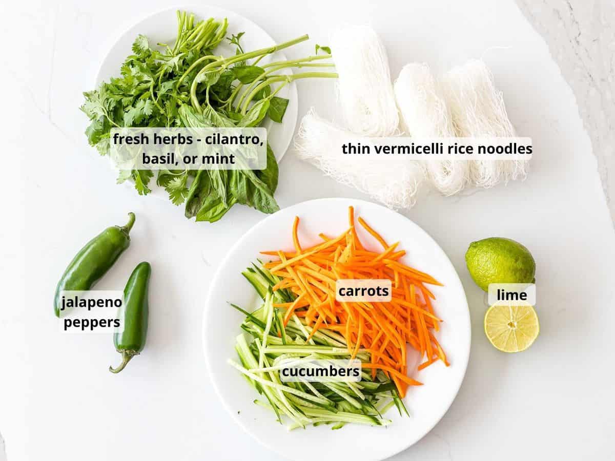 Ingredients for Vietnamese noodle salad including vermicelli rice noodles, fresh herbs, and vegetables on a white surface.