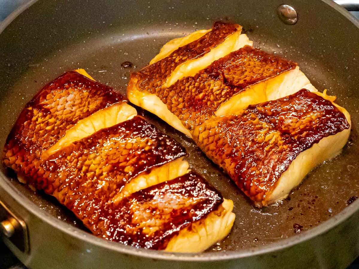 Sea bass filets being pan fried showing crispy, golden brown fried skin.