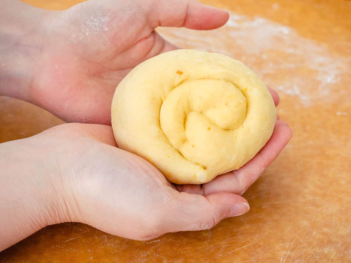 Sourdough pumpkin dough rolled into a round ball held by hands.
