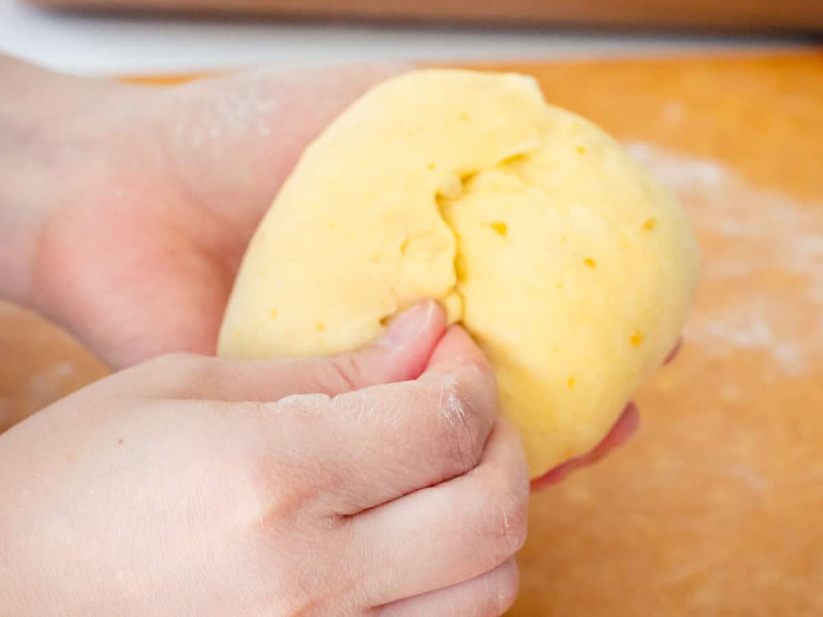 Hands pinching the seam of the dough closed to keep its form.