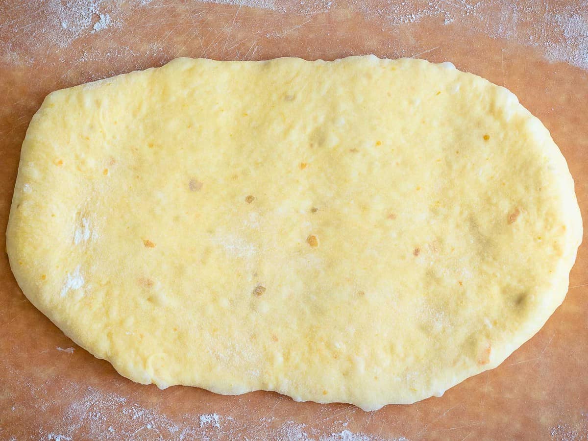 Pumpkin bread dough rolled into a flat oval shape on a wooden board.
