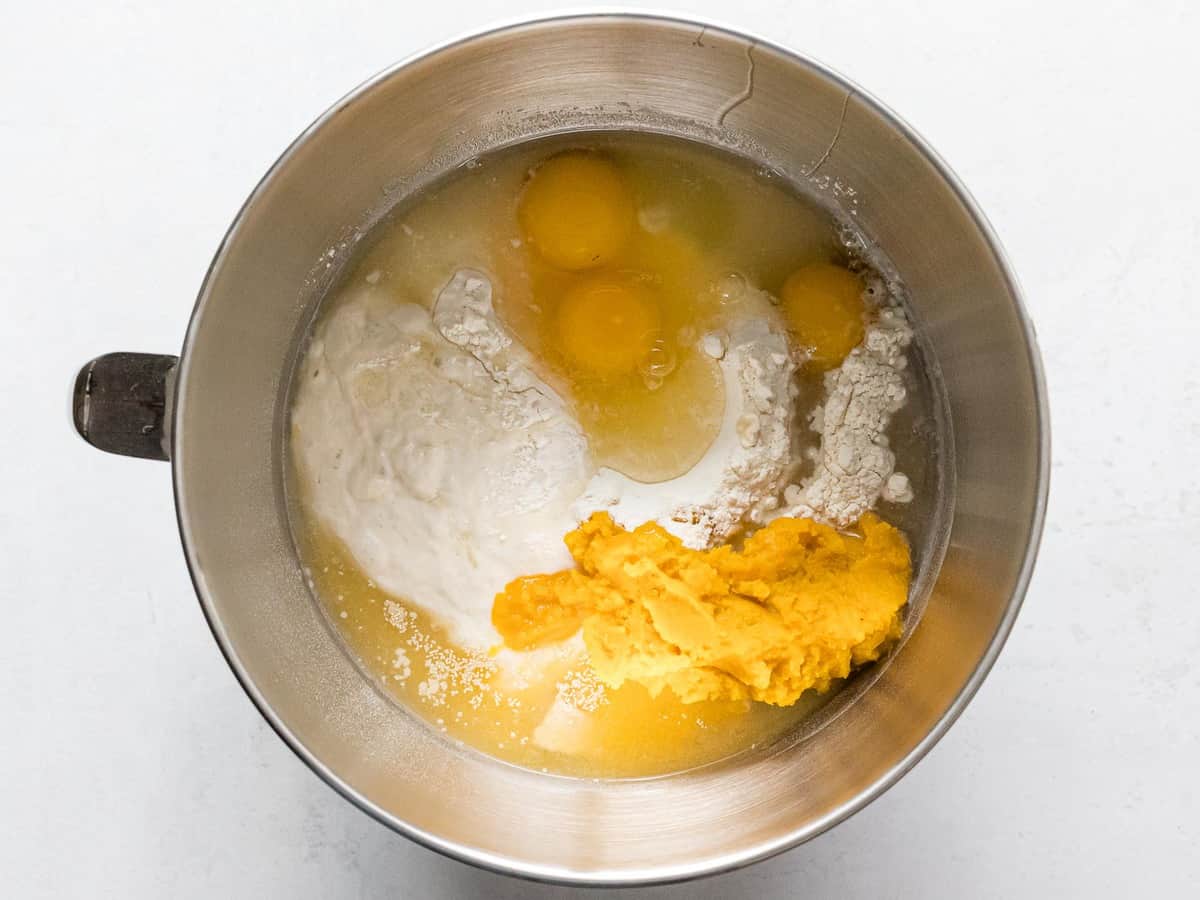 A metal stand mixing bowl with flour, eggs, mashed pumpkin, and other ingredients for pumpkin sourdough bread.