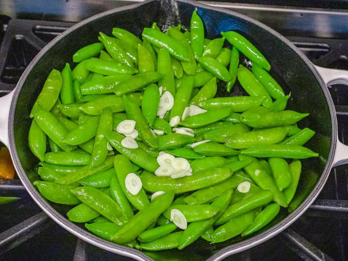 Sugar snap peas with garlic being sauteed in a dark pan.