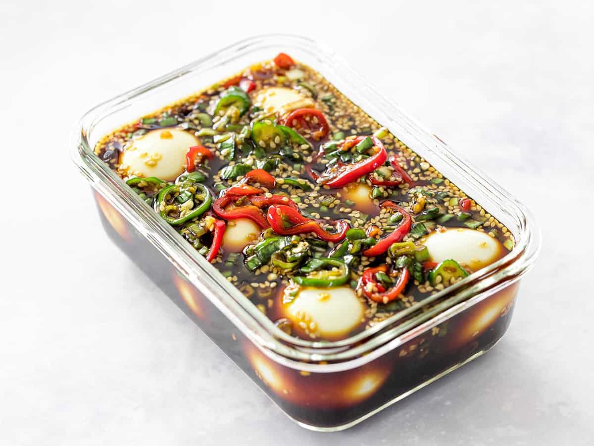 Soft boiled mayak eggs marinating in soy marinade with red and green peppers in a glass container.