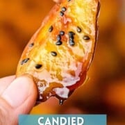 A piece of candied Korean sweet potato with black sesame seeds held by hand.