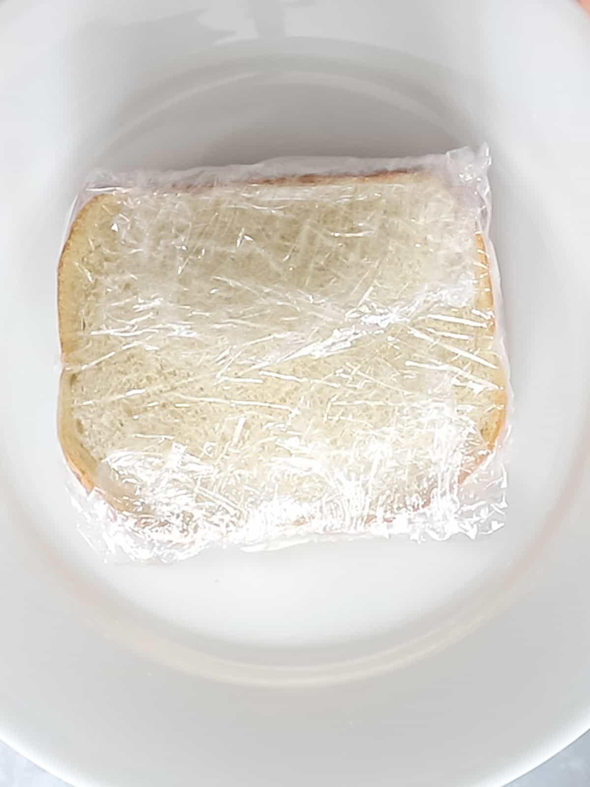 Japanese fruit sandwich wrapped in plastic wrap on a white plate.