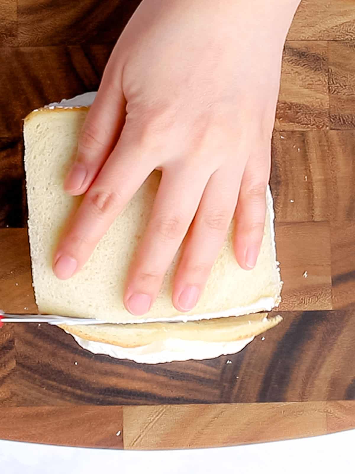 Cutting the crust off of white sliced bread laid on a wooden cutting board.