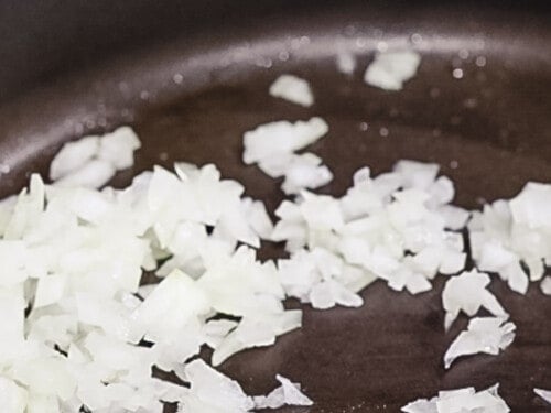 Diced white onions being sauteed in a pan.