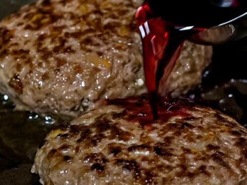 Red wine being added to Japanese hamburger steaks cooking in a pan.