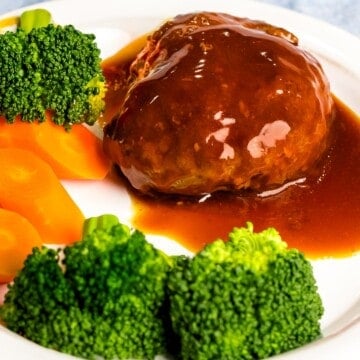 Japanese hamburger steak (hambāgu ハンバーグ) on a white plate next to broccoli and carrots.
