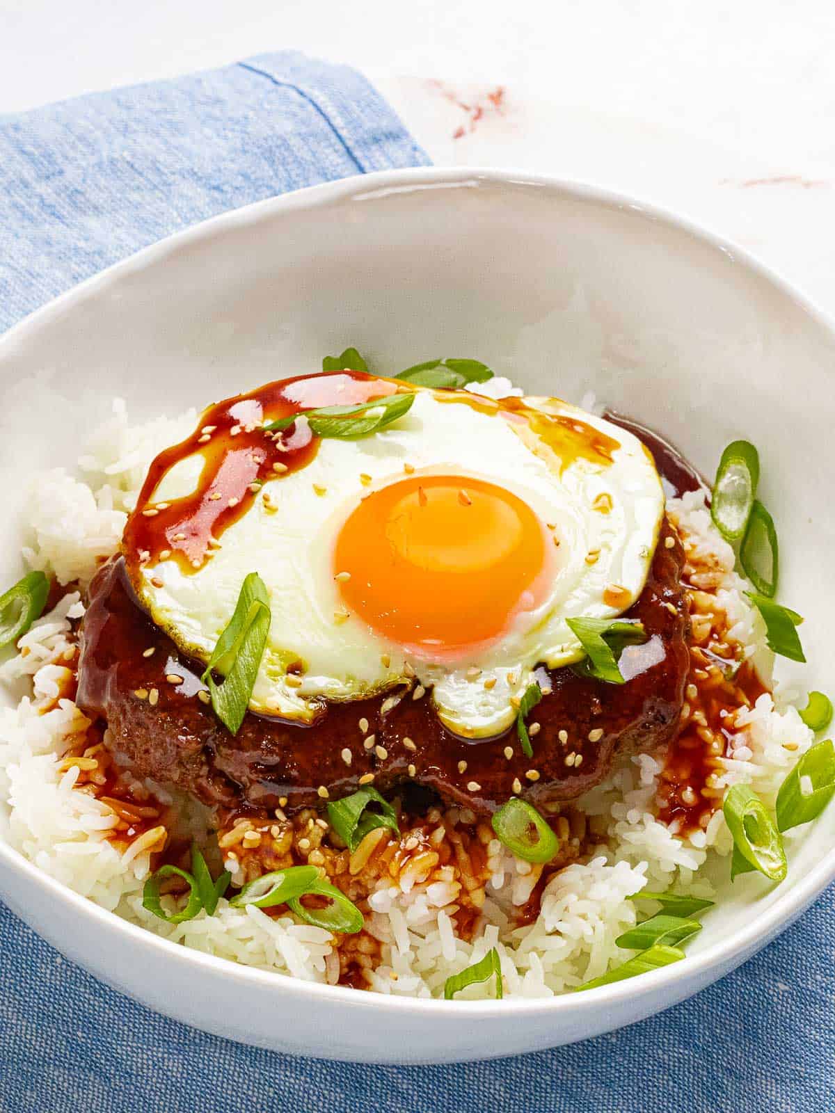 Hawaiian loco moco with a burger, gravy, white rice, and a sunny side up egg in a white bowl.