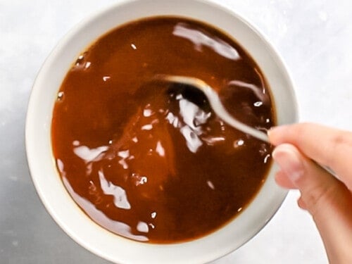 Brown gravy being mixed in a white bowl with a spoon.
