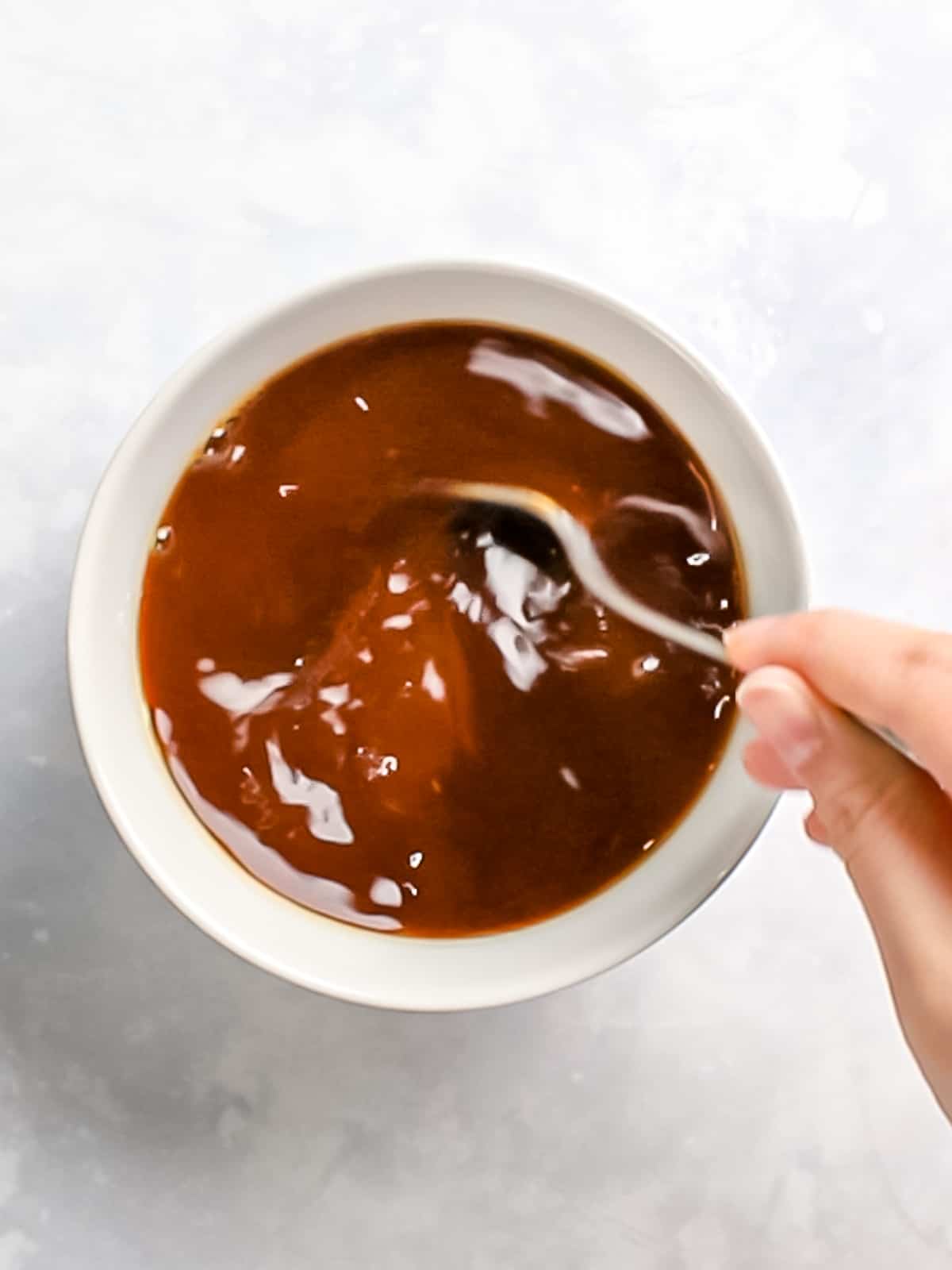 Brown gravy being mixed in a white bowl with a spoon.