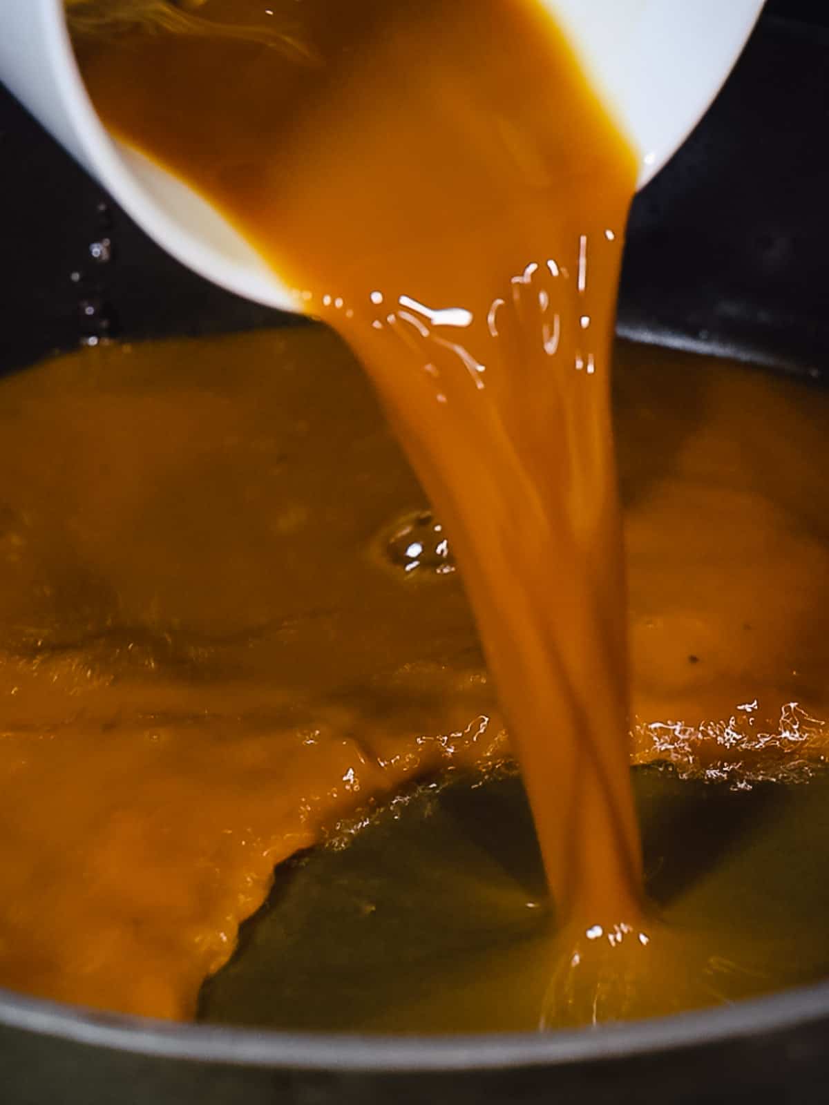 Brown gravy being poured into a pan.