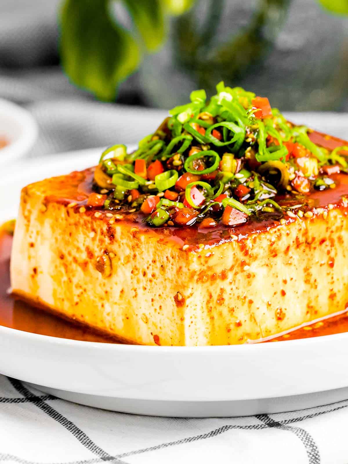 Korean silken tofu with vegan soy sauce with green onions, and red pepper flakes in a white bowl.